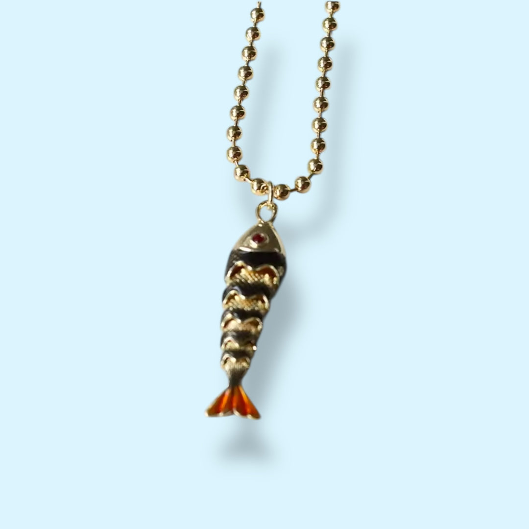 Gold fish-shaped pendant on a chain against a light blue background