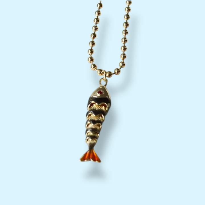 Gold fish-shaped pendant on a chain against a light blue background